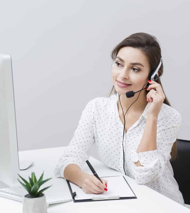 front-view-smiley-woman-writing-something-down-while-talking-headset
